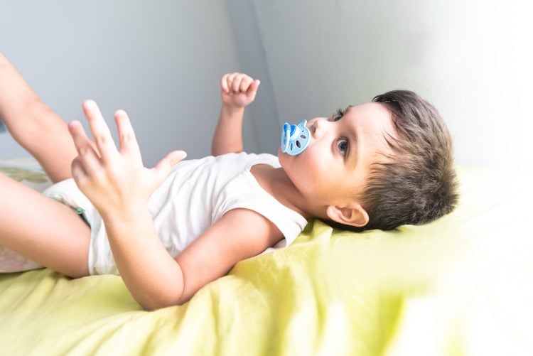 Baby boy in white t-shirt lying on bed