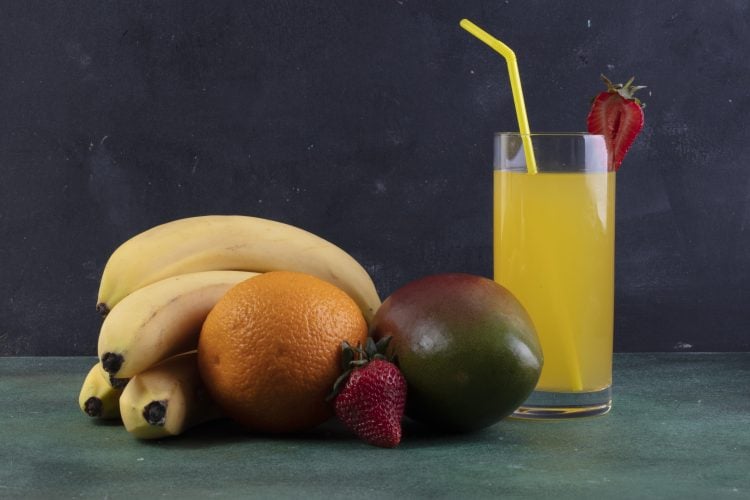 front view bananas with mango orange strawberries and a glass of orange juice